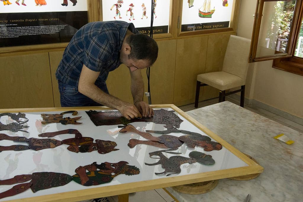Işıklı masaya eğilmiş, Karagöz tasvirlerini tek tek yerleştiren bir usta