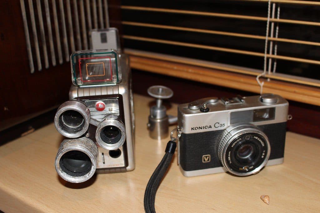 Ahşap bir masanın üzerinde yan yana duran eski analog fotoğraf makineleri ve objektifler
