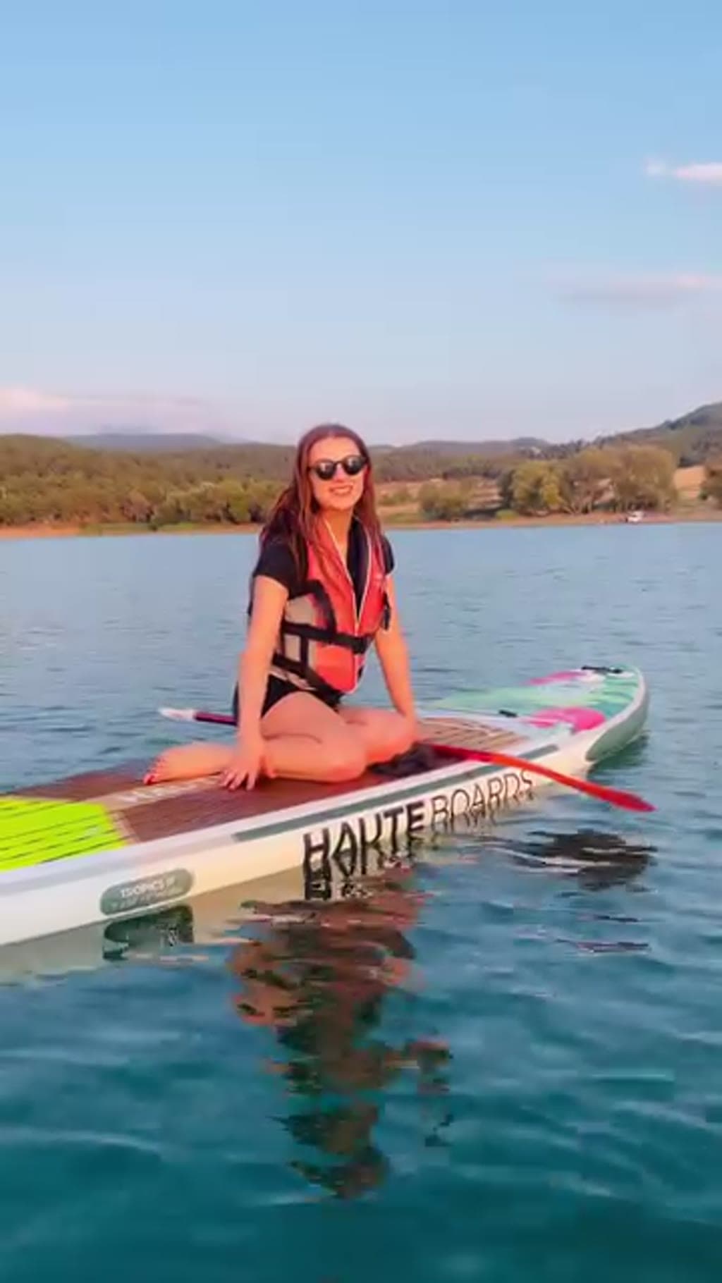 Sakin gölde stand up paddle tahtasının üstünde oturan kişi